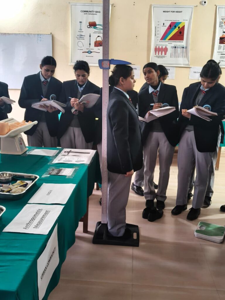 Nursing student undergoing height and weight assessment for BMI calculation on a clinical stadiometer during a health assessment practical